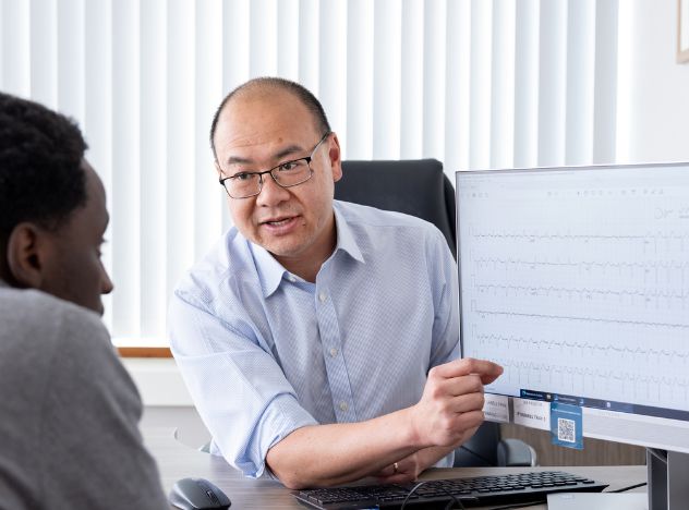 Cardiac surgeon with patient looking at heart rhythm on computer