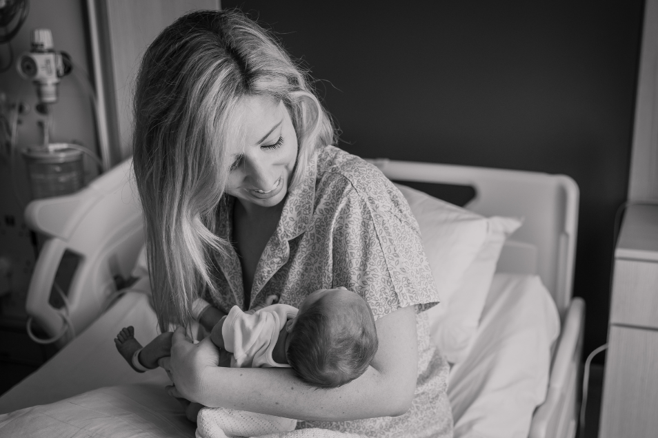 Mother sits in hospital bed smiling and cradling her baby.