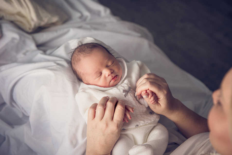 A mothers holds her baby hands whilst cradling the baby in her lap.