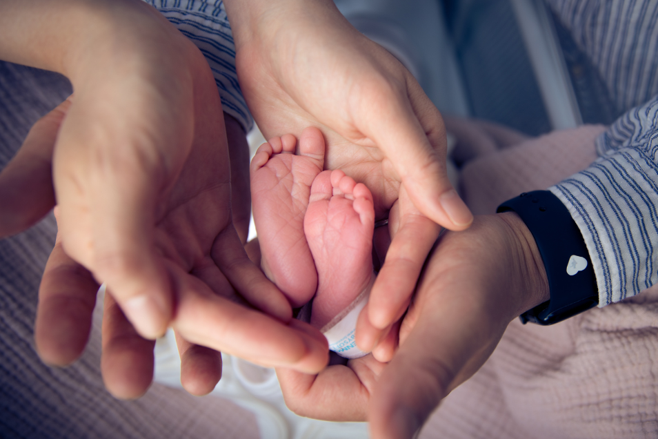 The parents hands wrap around their baby's feet.